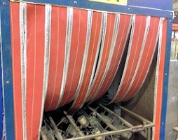 Red and clear high-temperature oven strip curtains hanging over an industrial conveyor oven, providing flexible heat containment and easy access for workers.