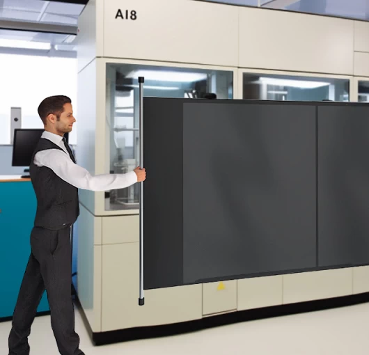 Retractable industrial separation curtain mounted on a fixed frame, shown partially extended to divide machinery areas within a manufacturing environment.