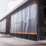 Large industrial warehouse curtains covering a wide exterior opening, transparent PVC strip curtains used for weather control and visibility