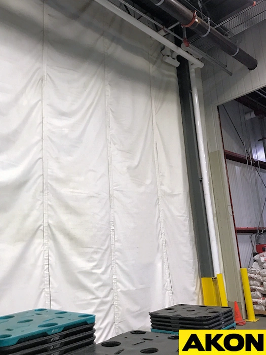 White insulated industrial curtain wall installed inside a warehouse to provide temperature separation and reduce heat loss between work areas.